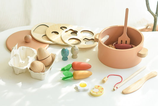 Set of wooden toys including a pot, utensils, and food items on a white surface.