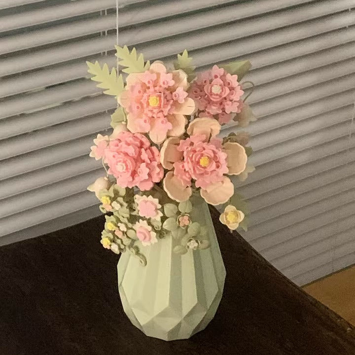 Decorative vase with pink flowers against a window with blinds