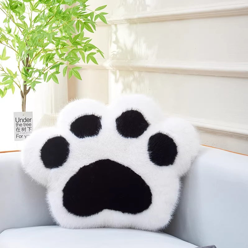 White paw-shaped pillow on a white couch with a plant in the background
