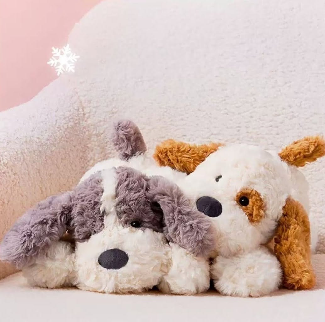 Two plush dogs sitting together on a soft surface with a pink background
