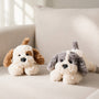 Two plush dog toys, one white with brown ears and one gray with black ears, on a light-colored couch.