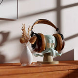 Headphones on a unique stand with a decorative figure, placed on a wooden surface.