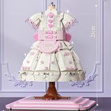 Fully assembled Lolita dress ornament displayed on a wood desk beside books, showing finished scale and layered ruffle structure