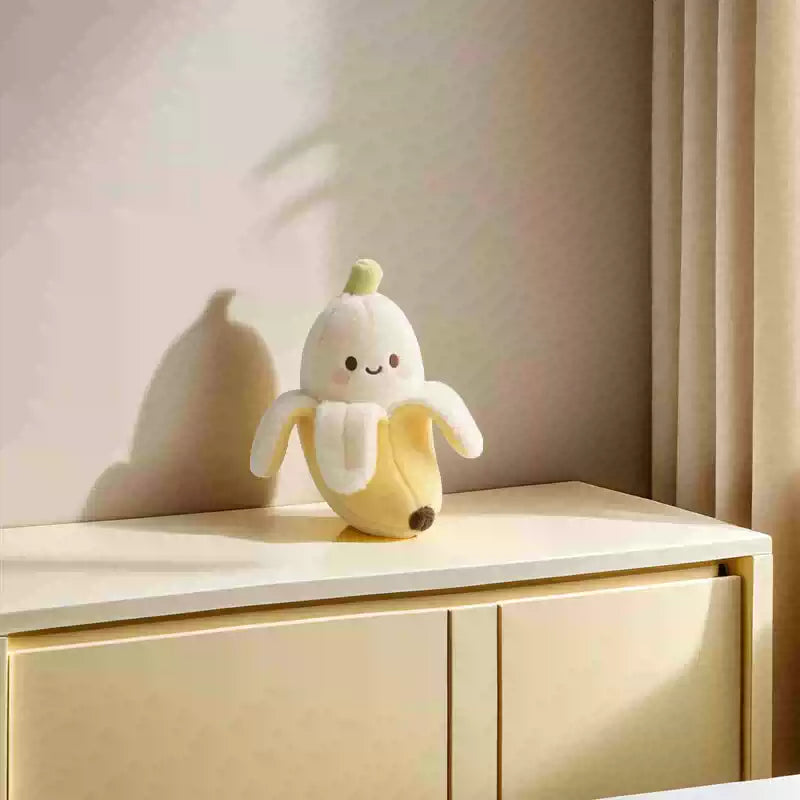 Plush toy banana with a smiling face on a wooden surface with a soft pink background