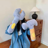 Person holding large plush wrench and hammer in a room with a wooden dresser and lamp.