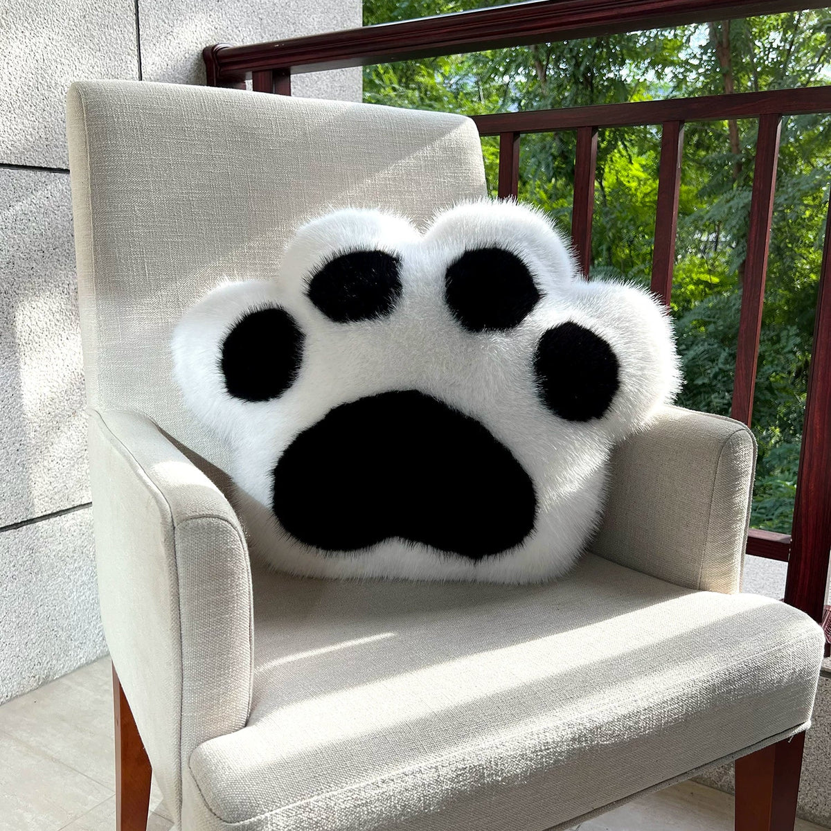 White paw-shaped pillow on a chair with a balcony and greenery in the background