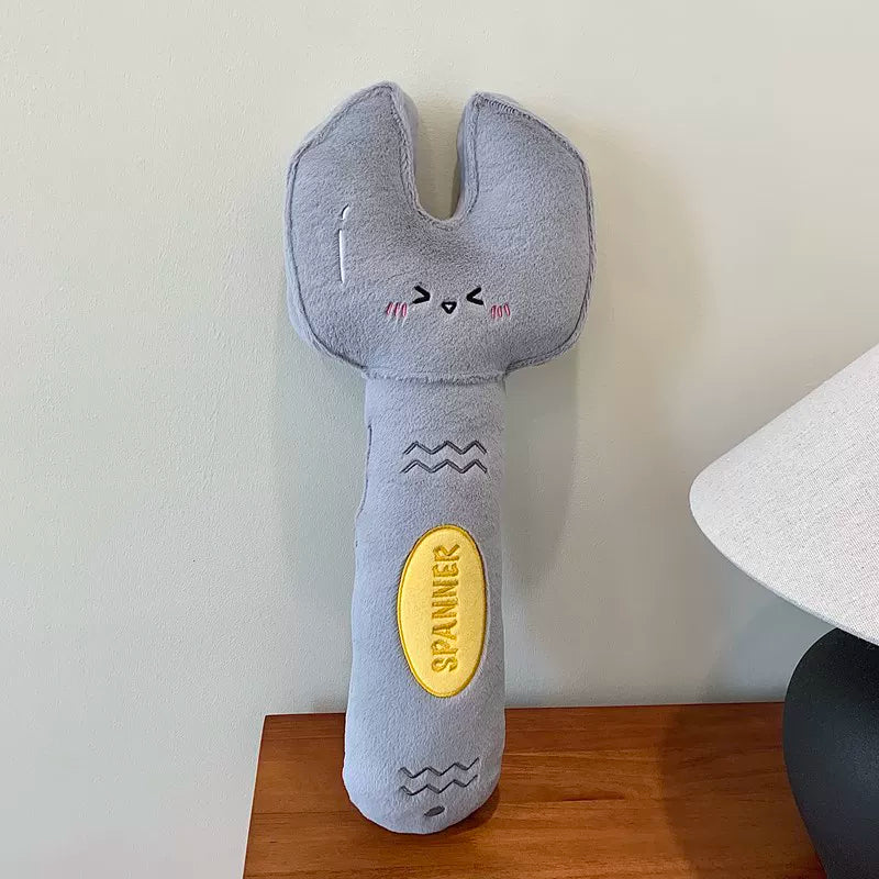 Plush wrench toy with a face on a wooden surface and white background