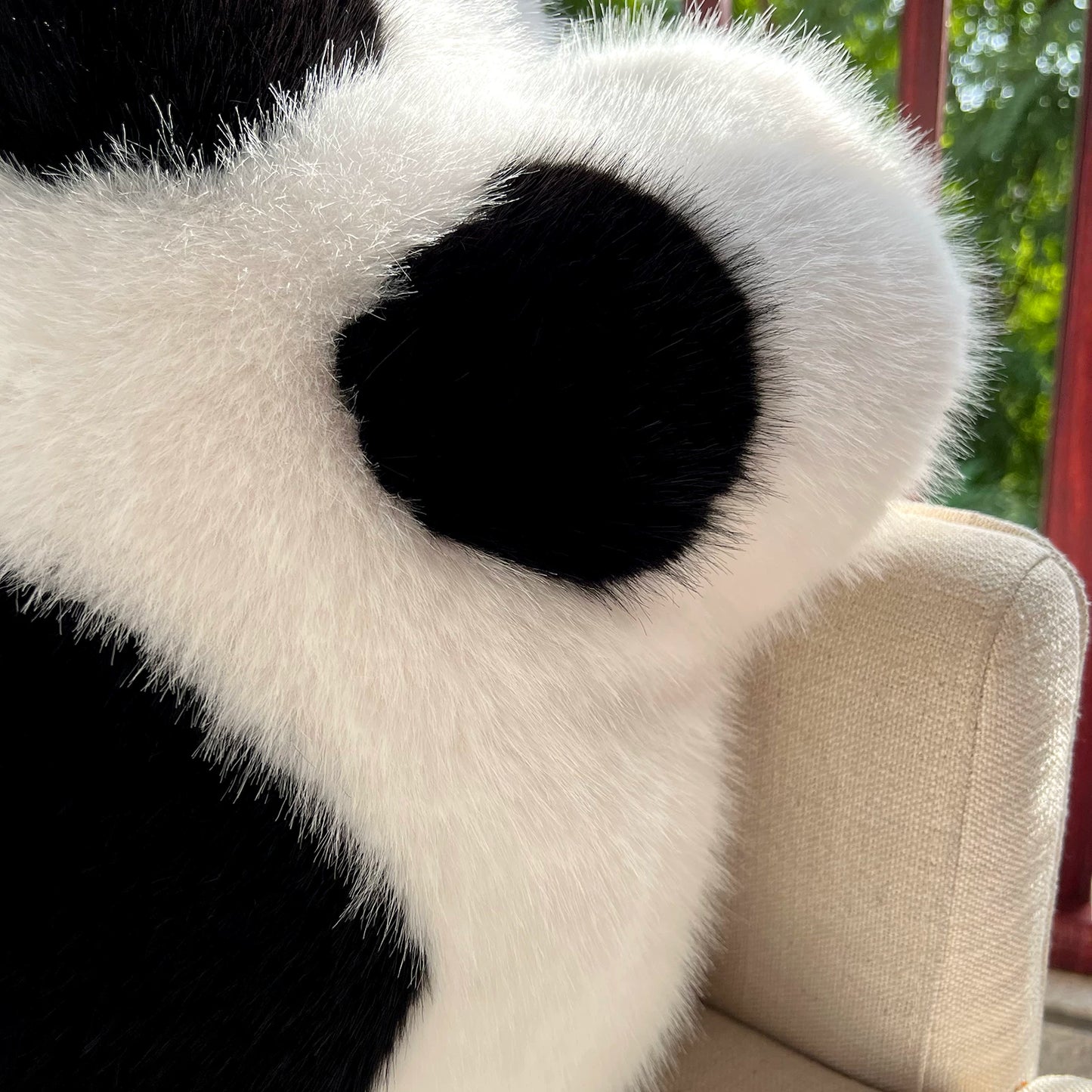 Close-up of a plush panda toy on a beige chair with a blurred green outdoor background