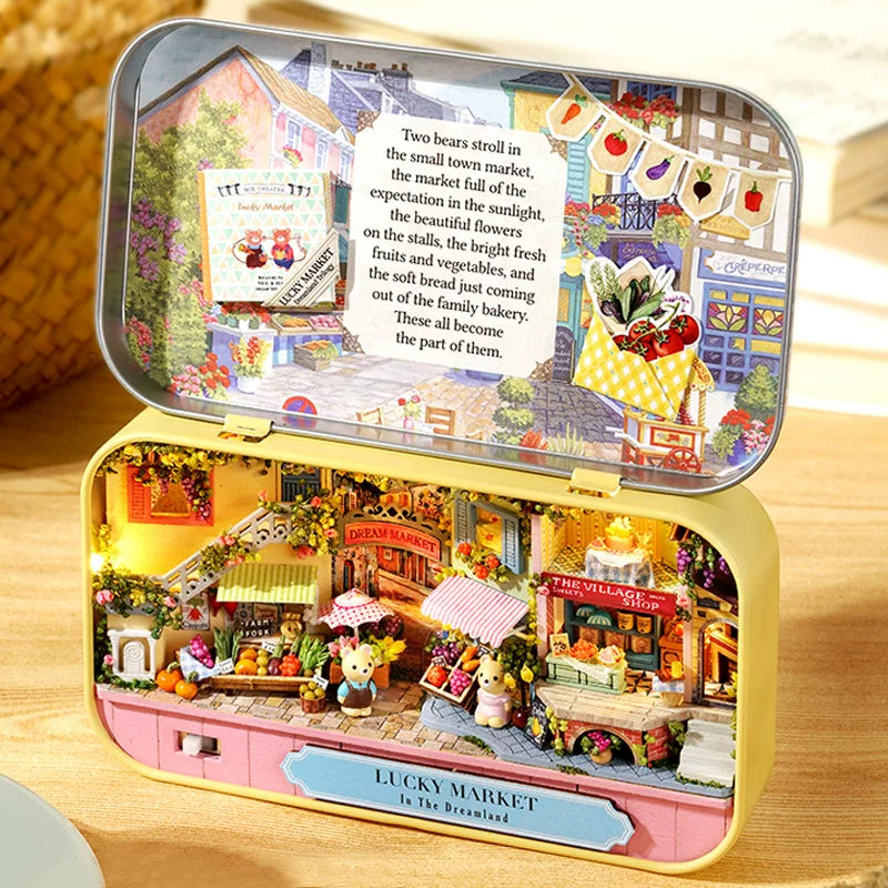 Miniature model of a market scene inside an open tin box on a wooden surface.
