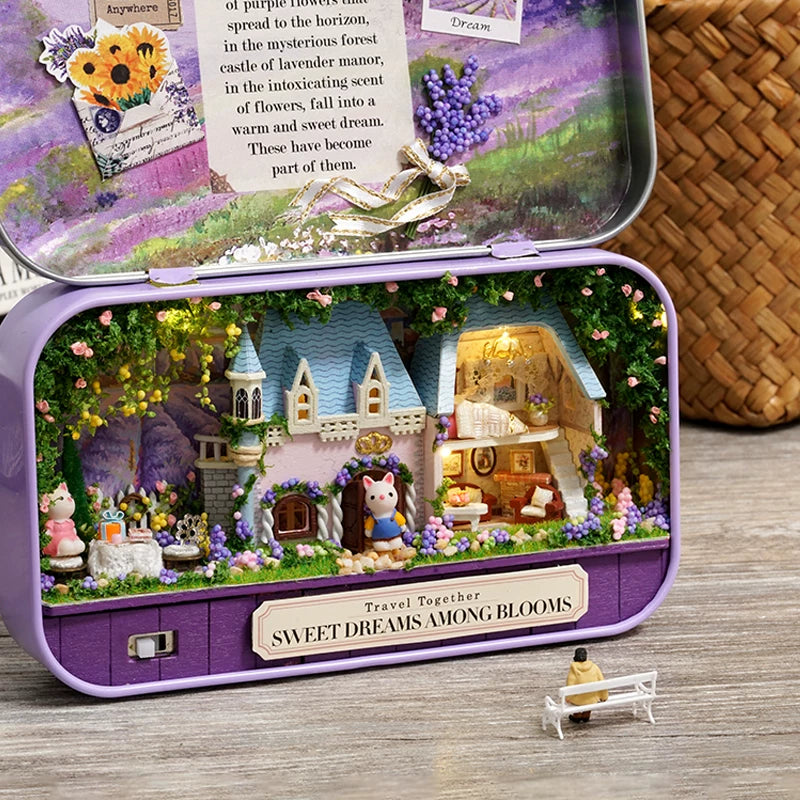 Miniature fairy garden inside a purple tin with a castle and small figures on a wooden surface.