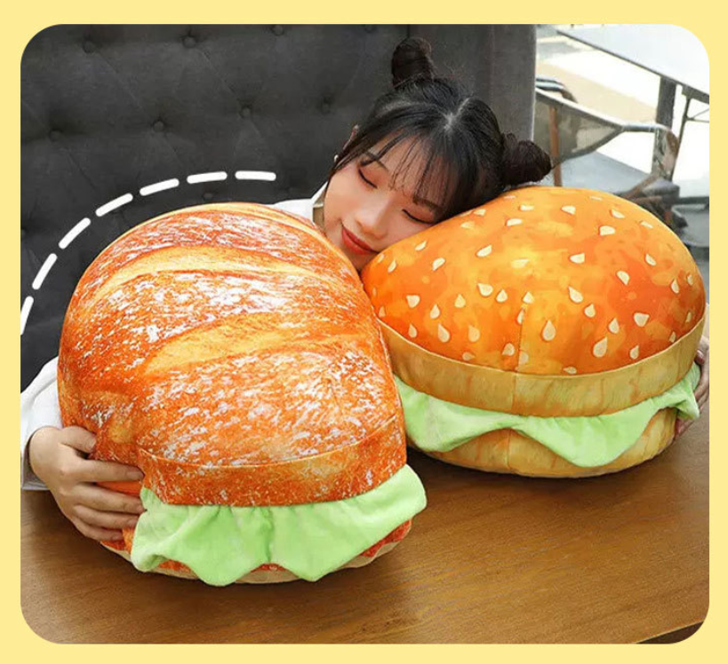 Person hugging a large plush burger and bread toy on a wooden table.