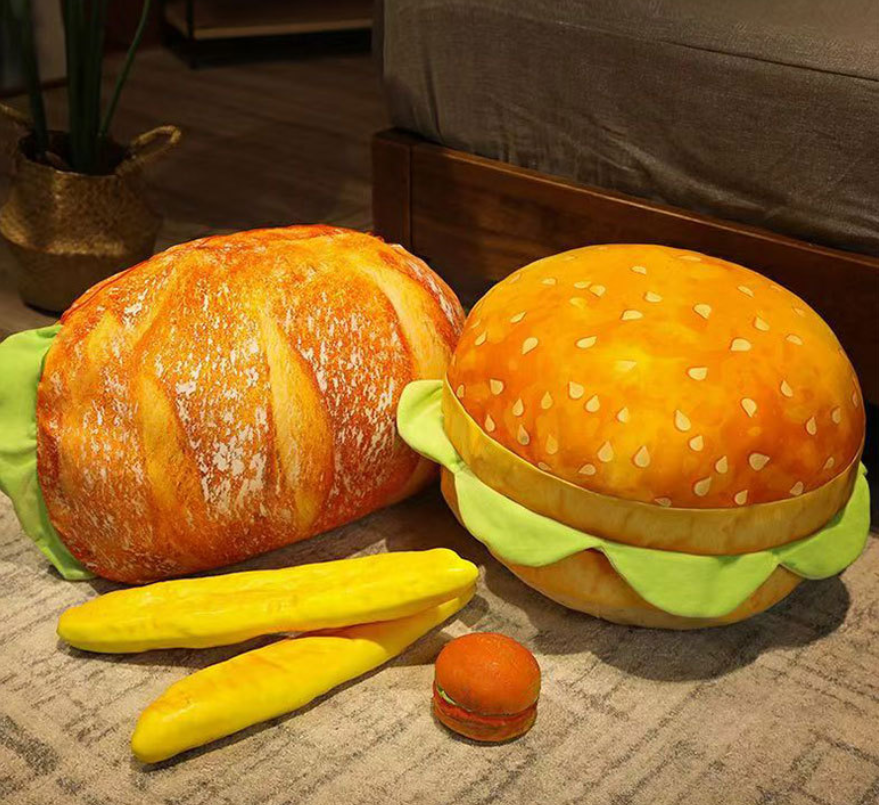 Hamburger-shaped plush toy with buns, lettuce, and a cherry on a textured surface.