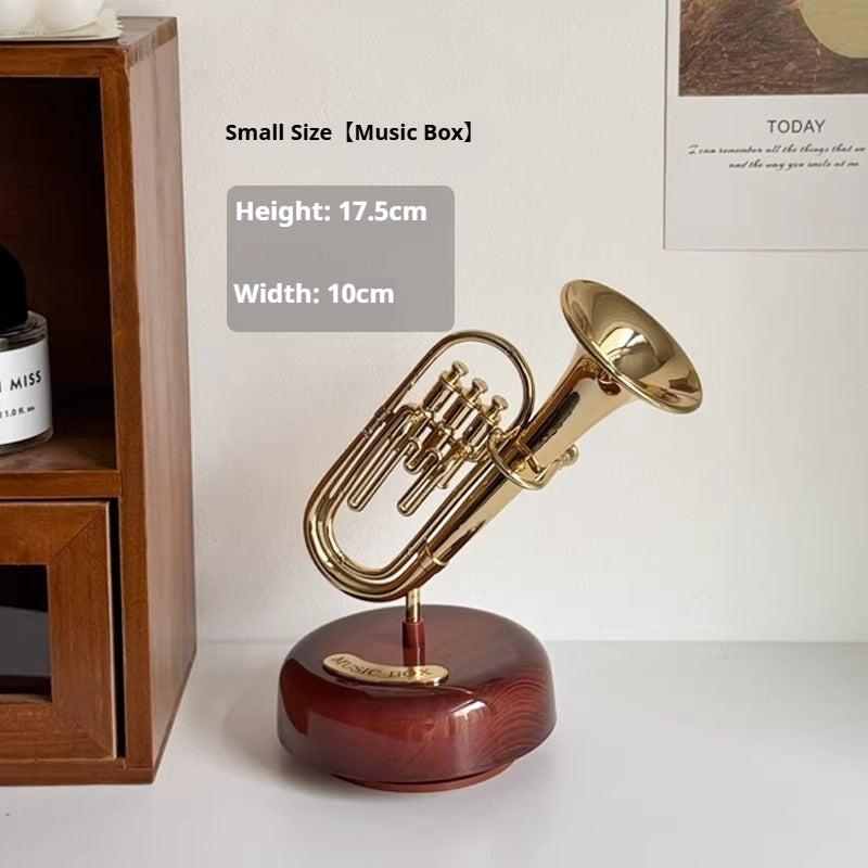 Small size music box with gold trumpet design on a wooden base, placed on a white surface.