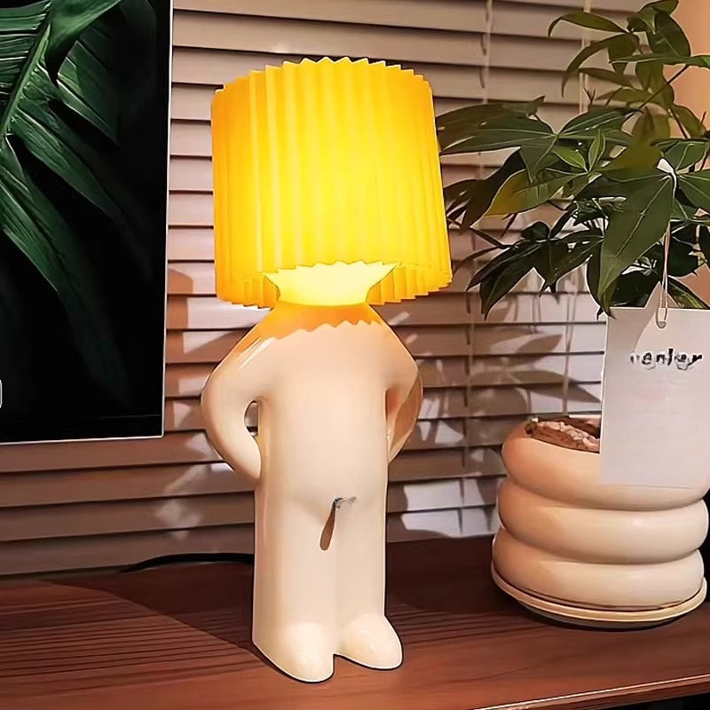 Yellow lamp with a white base on a wooden surface, surrounded by plants.