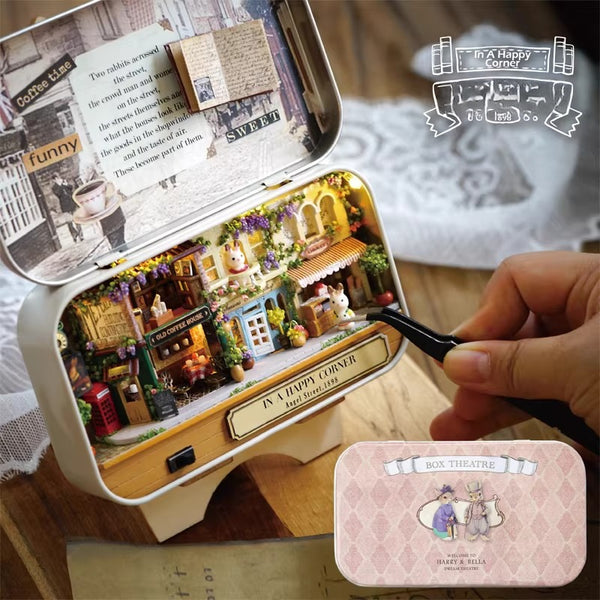 Miniature model of a town inside a tin box with 'A Happy Corner' label, held by a hand.