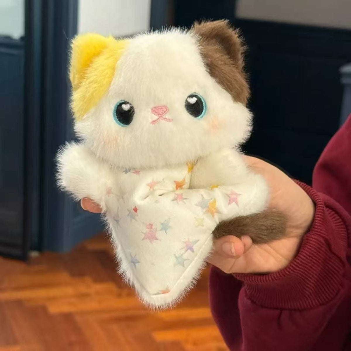 Plush toy resembling a cat held in a hand with a star-patterned blanket