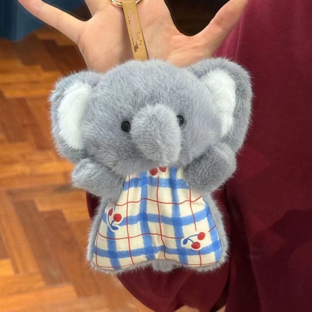 Plush elephant toy with a checkered dress held by a hand.