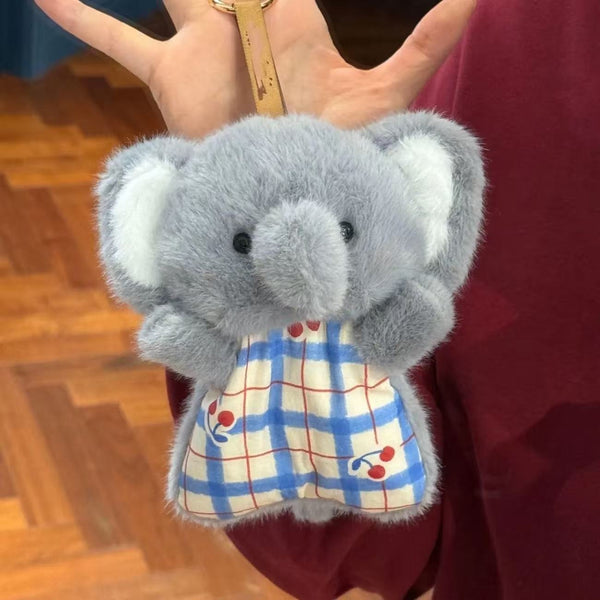 Plush elephant toy with a checkered dress held by a hand.