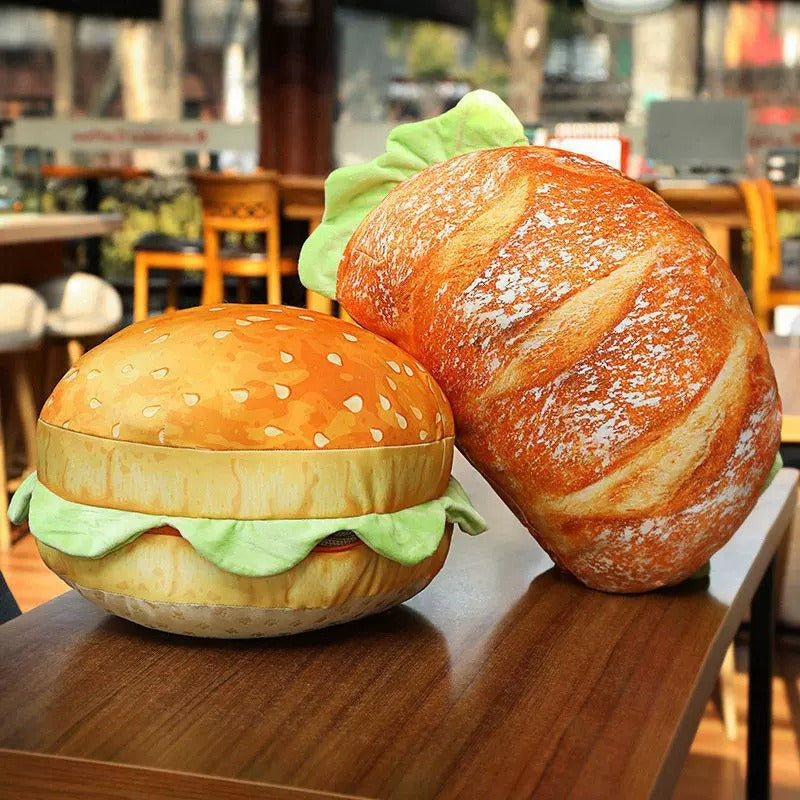 Two plush toys shaped like a hamburger and a loaf of bread on a table.