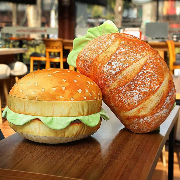 Two plush toys shaped like a hamburger and a loaf of bread on a table.